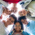 Low angle view of young trendy friends hugging, smiling and making a circle with their heads.
