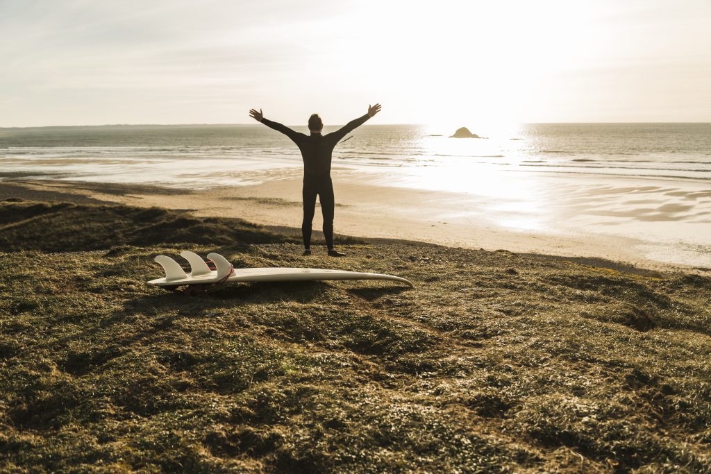 France, Bretagne, Finistere, Crozon peninsula, man at the coast with outstretched arms and surfboard