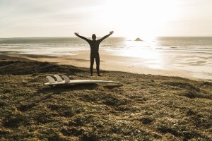 France, Bretagne, Finistere, Crozon peninsula, man at the coast with outstretched arms and surfboard