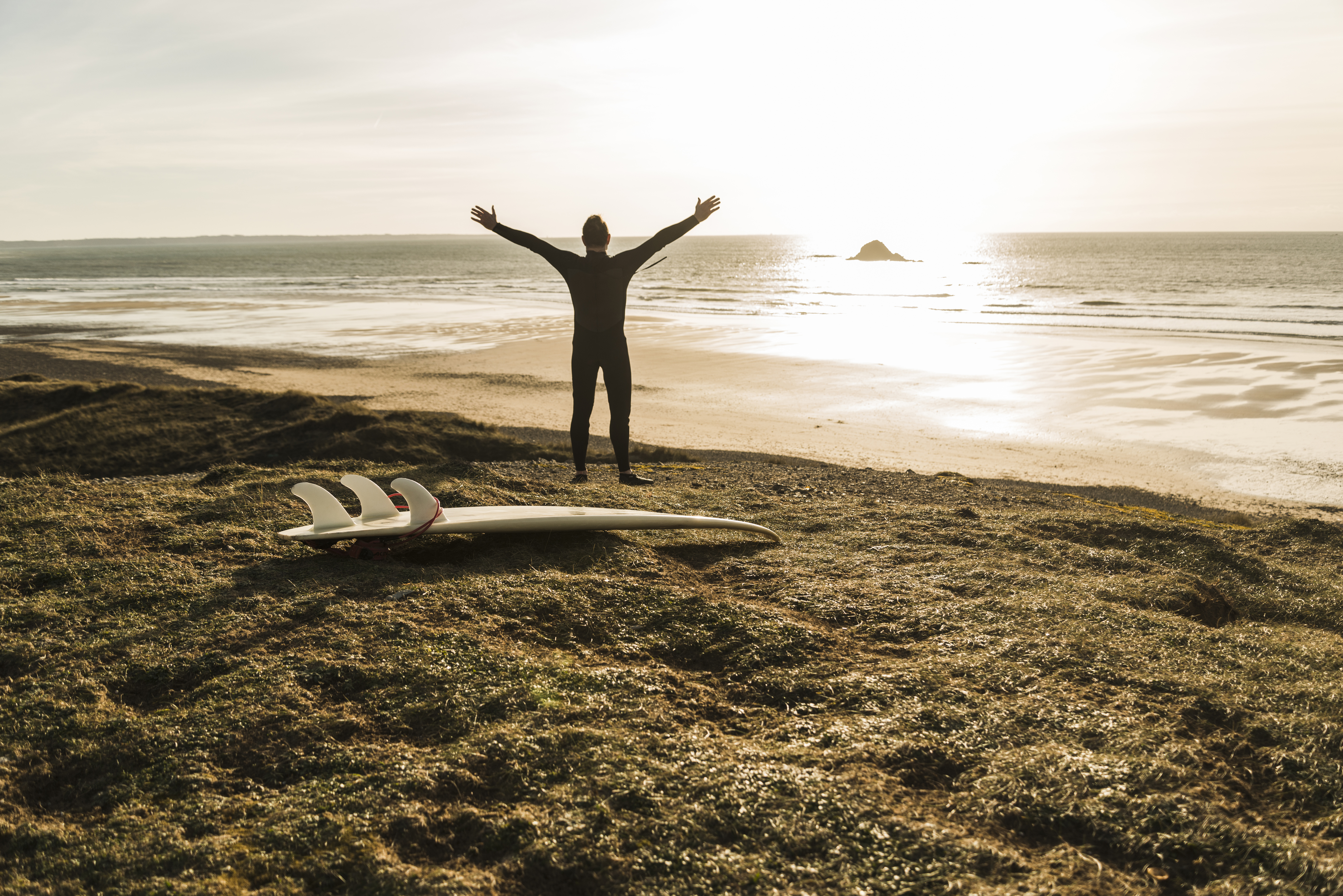 France, Bretagne, Finistere, Crozon peninsula, man at the coast with outstretched arms and surfboard