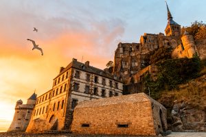 Seagulls flying over dramatic sunset in Mont Saint-Michel, Normandy, France.